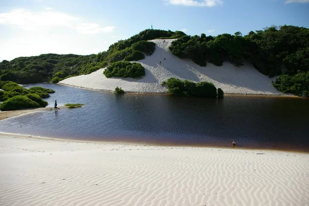 Laguna de agua oscura rodeada de dunas y vegetación